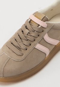 Baskets en suède beige avec des accents en cuir rose, lacets beige plats et semelle en caoutchouc texturée. Logo notable sur la languette.