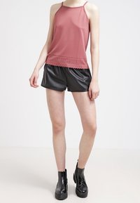Top rosa senza maniche con bordi all'uncinetto, abbinato a pantaloni corti in faux pelle nera e stivali neri con tacco chunky. Tessuti dal tocco morbido.