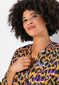 Zwarte blouse met levendige oranje, paarse en witte abstracte patronen. Heeft een knoopsluiting aan de voorkant en een zachte stoffen textuur.