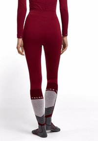 Persoon gekleed in strakke kastanjebruine leggings en bijpassende top met lange mouwen, met grijze en kastanjebruine kniehoge sokken met het label "FALKE", gezien van achteren.