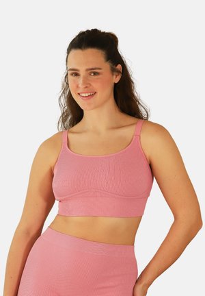 Woman with long brown hair wearing a matching pink ribbed crop top and high-waisted skirt, smiling with one hand on her hip.