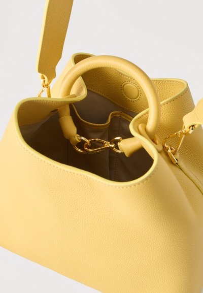 Κίτρινη τσάντα από δερματίνη με στρογγυλές λαβές, αποσπώμενο λουρί ώμου, χρυσά κλίπς και ανοιχτό πάνω μέρος που αποκαλύπτει εσωτερικές θήκες.