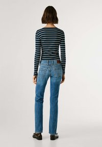 Haut à rayures bleu marine à manches longues et jeans droits bleus avec un patch en cuir ; tissu lisse, design décontracté, poches arrière simples et détails minimaux.