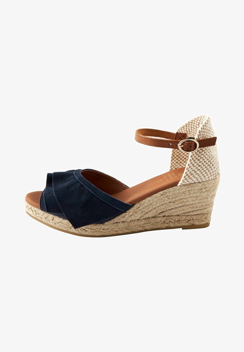 Tengerész kékszínű velúr wedge szandál, fonott sarokkal, nyitott orral és bokapánttal. Jellemzője az összegyűrt elülső dizájn és a természetes árnyalatú fonott középtalp.