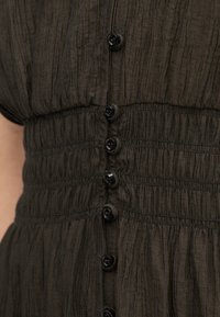 Robe vert foncé avec des plis verticaux, doté d'une taille cintrée et de boutons noirs sur le devant. Tissu doux et texturé avec un détail élastique.