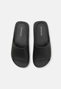 Sorte sandaler med glatt tekstur, åpen tå-design og polstret såle. Har preget merkevarelogo på innersålen.