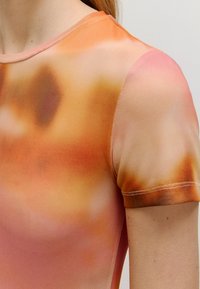 Kurzärmeliges Oberteil aus einem weichen, leichten Stoff mit einem Farbverlauf in warmen Orange-, Pink- und Brauntönen und einer glatten Textur.
