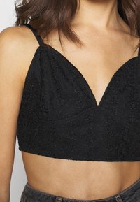 Black crop top with thin adjustable straps, featuring a textured floral pattern and a deep V-neck design.