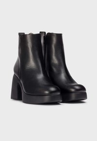Botas de tobillo de cuero negro con puntera redondeada, tacón grueso y cremallera lateral. Textura suave sin patrones o acentos visibles.
