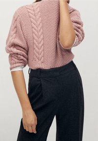 Gruby, różowy sweter na drutach z wzorem warkocza, zestawiony z ciemnymi, wysokim stanem spodniami. Bluza ma luźny krój i podwinięte rękawy.