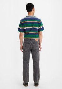 Camisa de manga corta a rayas en verde, azul, naranja y blanco combinada con jeans de mezclilla gris. Presenta un ajuste estándar y detalles sutiles en los herrajes.