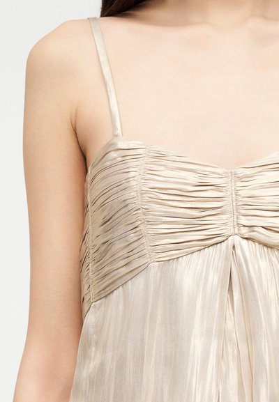 Κοντινό πλάνο ενός ατόμου που φορεί ένα φόρεμα σατέν σε απόχρωση σαμπάνιας με λεπτές τιράντες και λεπτομέρειες ρίγας στο σώμα.