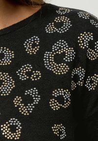 Schwarzes Shirt aus strukturiertem Stoff, verziert mit goldenen und silbernen Strassleopardenflecken, die ein gemustertes Design ergeben.