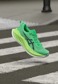 Green athletic shoe with a textured mesh upper, white sole, and a distinctive zigzag pattern on the side. Lightweight and streamlined design.