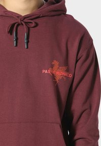 Felpa borgogna con grafica frontale arancione "PAS DE MONACO", tessuto morbido, cordoncini con punte nere e tasca a marsupio.