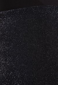 Černý oděv s texturovaným povrchem a malými, reflexními stříbrnými akcenty, které vytvářejí třpytivý efekt. Materiál vypadá jako tkaný a pružný.