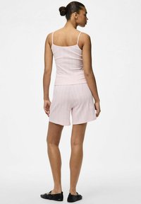 Top rosa claro de canalé con tirantes finos, combinado con pantalones cortos holgados a juego. Presenta un tejido texturizado y un ajuste casual. Zapatos planos negros.
