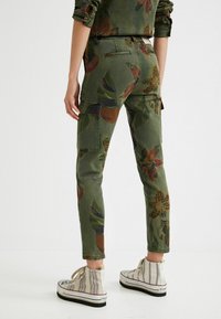 Cargo byxor i grön med blommönster, med sidofickor och en avsmalnande bendesign, kombinerat med beige randiga hög-top sneakers.