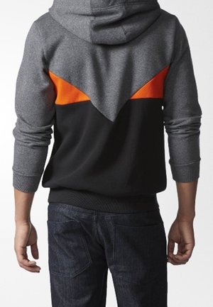 Felpa con cappuccio grigia e arancione; presenta un design triangolare arancione sulla schiena, polsini e orlo a costine. Indossata con jeans scuri.