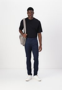Fekete rövid ujjú póló, tengerészkék slim-fit nadrág, fehér sportcipő és világosszürke oldaltáska. Egyszerű, modern dizájn, minta nélkül.