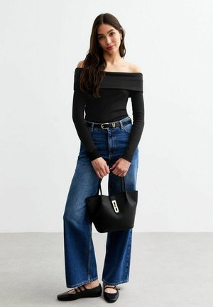 Schwarzes schulterfreies Oberteil, hochtaillierte blaue Jeans, schwarze flache Schuhe und eine strukturierte schwarze Handtasche mit goldener Verschlussdetail.