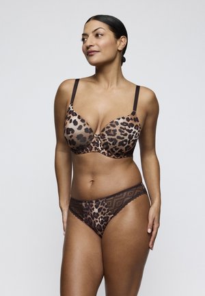 Woman wearing leopard print bra and matching panties with lace details, standing against a plain light gray background, facing slightly left.