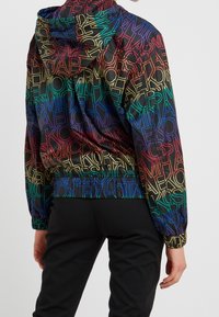 Giacca con cappuccio colorata caratterizzata da un gradiente di lettere di vari colori su uno sfondo nero. Polsini e vita elastici per un look aderente.