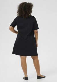 Vestido negro de manga corta con un ajuste relajado, hasta la rodilla, de tela de algodón suave y con un escote redondo, combinado con zapatos planos negros.