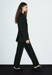 Black tailored suit with a long blazer and wide-leg pants, paired with pointed black shoes. Smooth texture and structured design.