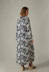 Svart och vit lång klänning med ett svängande mönster; har långa ärmar, rak skärning, sidoklyftor och ett lätt tyg. Bärs med espadrill-platåer.