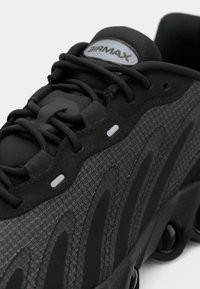 Sapatilha esportiva preta com tecido cinza texturizado, almofada proeminente e atacadores escuros. Apresenta um logo prata "AIRMAX" na língua.