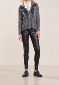 Suéter gris con cremallera y acentos bordados en negro, combinado con leggings de cuero negros y zapatos de cordones negros con tachuelas. Textura suave.