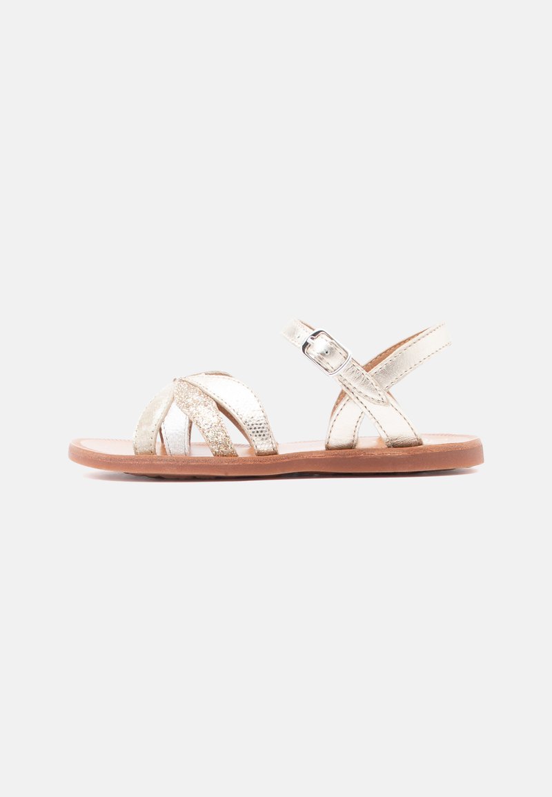 Επίπεδη σανδάλι με μεταλλικούς χρυσούς ιμάντες, λαμπερό μπροστινό ιμάντα, ρυθμιζόμενο αγκράφα και καφέ σόλα, εμφανίζεται σε πλευρικό προφίλ.