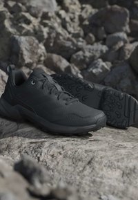 Black trail running shoes with rugged soles placed on rocky terrain, highlighting durability and outdoor use.