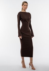 Abito midi marrone a coste con maniche lunghe, scollatura a barca e silhouette aderente. Realizzato in un morbido tessuto testurizzato con una finitura elegante.