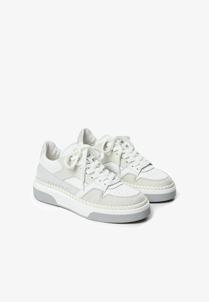 Fehér sneaker velúr és bőr felsőrésszel, kerek orral, vastag fehér talppal és szőtt részlettel a talp mentén. Fűzők és párnázott nyelv tartozik hozzá.