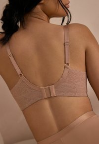 Lichtbeige bh met kant achterkant ontwerp, verstelbare bandjes en haak-en-oogsluiting. Gladde textuur met delicate bloemenpatroon.