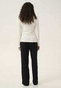 Cremiges Langarmoberteil mit strukturiertem Blumenmuster, kombiniert mit schwarzen weiten Hosen. Das Outfit zeigt von hinten eine taillierte Silhouette.