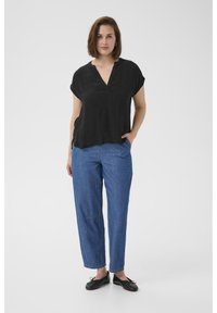 Haut noir à manches courtes avec un col en V, associé à un jean fuselé bleu clair avec des coutures visibles et des ballerines noires.