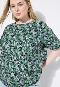 Camiseta de manga corta con estampado floral que presenta un fondo negro con flores moradas y azules. Tejido ligero, corte suelto y escote redondo.