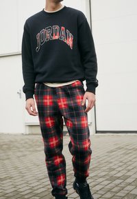 Sudadera negra con el logo "JORDAN", combinada con pantalones de cuadros en rojo y negro que presentan un patrón de ajedrez, usados con calzado negro.