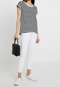 Černobíle pruhované tričko s ohrnutými rukávy, bílé skinny džíny, bílé tenisky a malou černou kabelku.