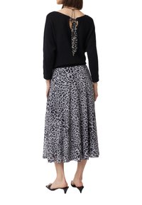 Schwarzer Pullover mit offenem Rücken und Knoten, kombiniert mit einem fließenden grauen Rock im Leopardenmuster und schwarzen Absatz-Mules.