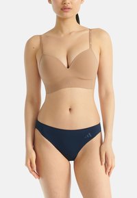 Naakte, gevormde beha met verstelbare bandjes, gladde textuur en logo-detail. Gecombineerd met marineblauwe lage bikini-slipjes, naadloos ontwerp.