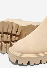 Bottes chelsea beiges avec une semelle en caoutchouc épaisse. Tige en suède douce et nez arrondi. Rainures profondes remarquables sur la semelle pour une meilleure adhérence.