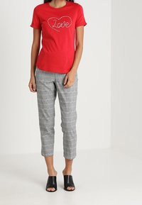 Camiseta roja de mangas cortas con gráfico de "Amor", combinada con pantalones cortos de cuadros grises y mule de punta abierta negros. Diseño sencillo y ajuste cómodo.