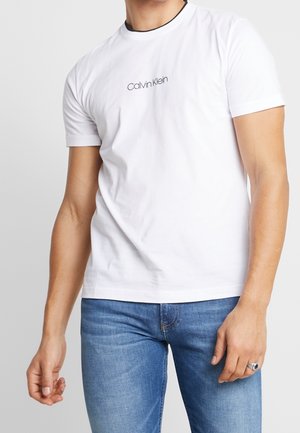 Witte katoenen T-shirt met ronde hals en korte mouwen, met een zwart geborduurd "Calvin Klein"-logo op de borst tegen een effen achtergrond.