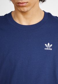 T-shirt en coton bleu marine avec un col rond, présentant un petit logo Adidas blanc avec trois accents de feuilles sur la poitrine gauche.