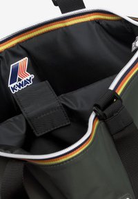 Interno di una borsa morbida verde con fodera nera, logo K-Way, fascia accentuata multicolore intrecciata e tracolla nera regolabile. Chiusura con cerniera.
