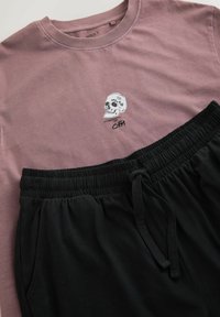 T-shirt en coton rose avec un motif de crâne et joggers à cordon de serrage noir. Les deux ont une texture douce et une coupe décontractée.
